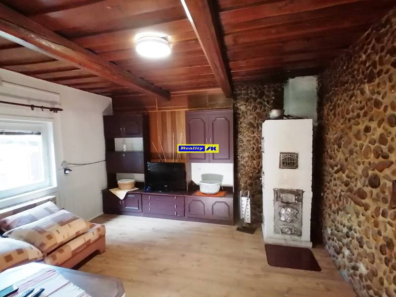 Obývacia izba v chate s kamennou stenou, pecou a dreveným stropom.