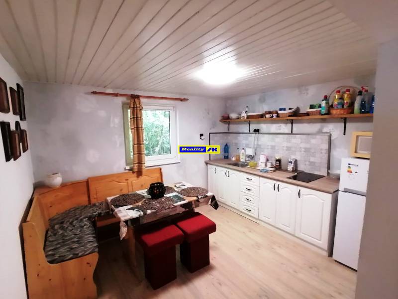 Kuchyňa v chate s posedením, bielou kuchynskou linkou, poličkami a oknom.