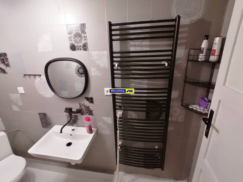 Kúpeľňa v chate so zrkadlom, umývadlom a rebríkovým radiátorom na stene.