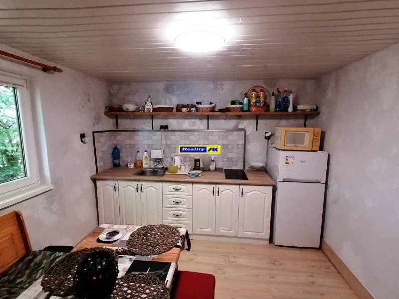Kuchynka v chate s dreveným nábytkom, poličkami a kuchynským vybavením, svetlá miestnosť.