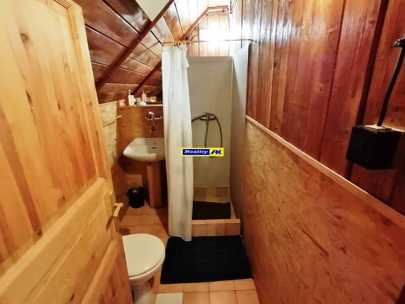 Drevený interiér malej kúpeľne s wc a sprchovacím kútom na chatke, ideálny pre relax.