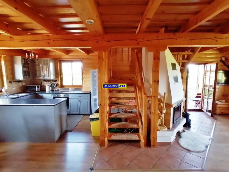 Interiér chaty so schodiskom, krbom a kuchyňou s drevenými prvkami.