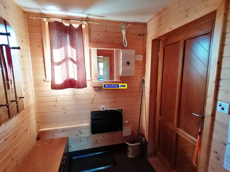Interiér chaty s drevenými stenami, oknom so záclonami a dverami z masívu.