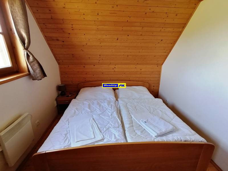 Spálňa v chate s dreveným obložením, jednoduchou manželskou posteľou a oknom.