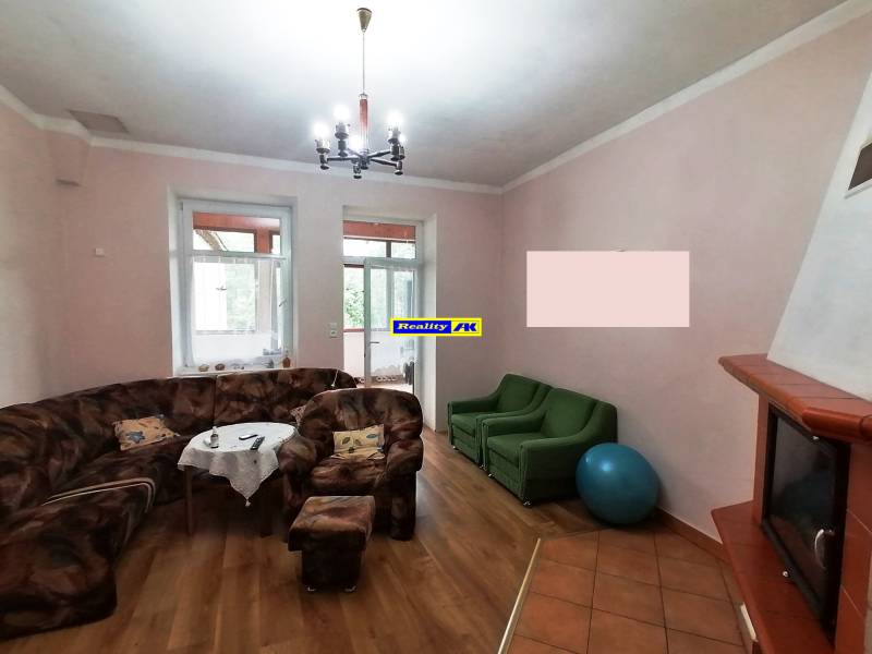 Obývačka v rodinnom dome s krbom, pohovkou, kreslami a dekoráciami na stenách.