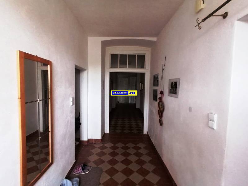 Chodba s dlaždicami a zrkadlom v rodinnom dome, steny zdobia obrazy.