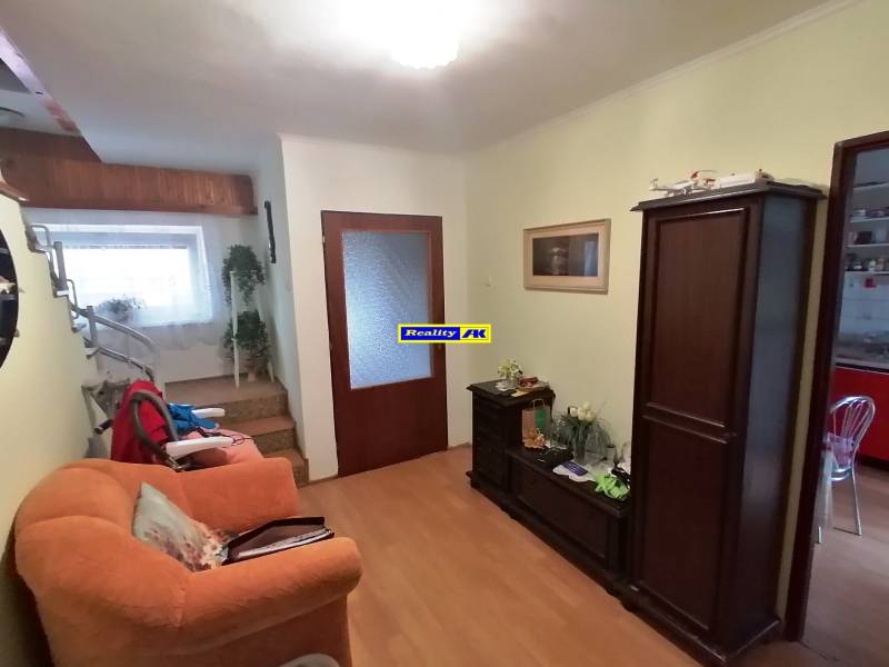 Interiér rodinného domu s oranžovým kreslom a schodiskom, podlaha s dreveným dekorom.