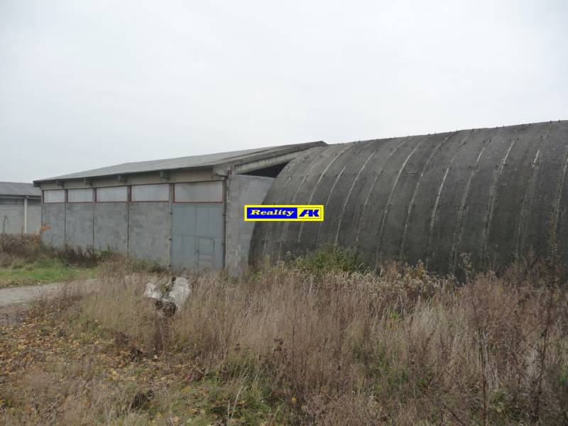 Priemyselné sklady a haly v Trnave s betónovými stavbami obklopené trávou a kríkmi.