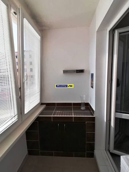 Zasklený balkón v 3-izbovom byte s tmavou dlažbou a skrinkou.