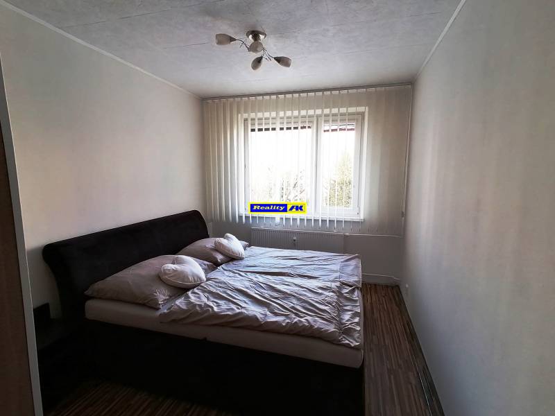 Spálňa s dvojlôžkovou posteľou, závesmi a podlahou s dreveným dekorom v 3-izbovom byte.