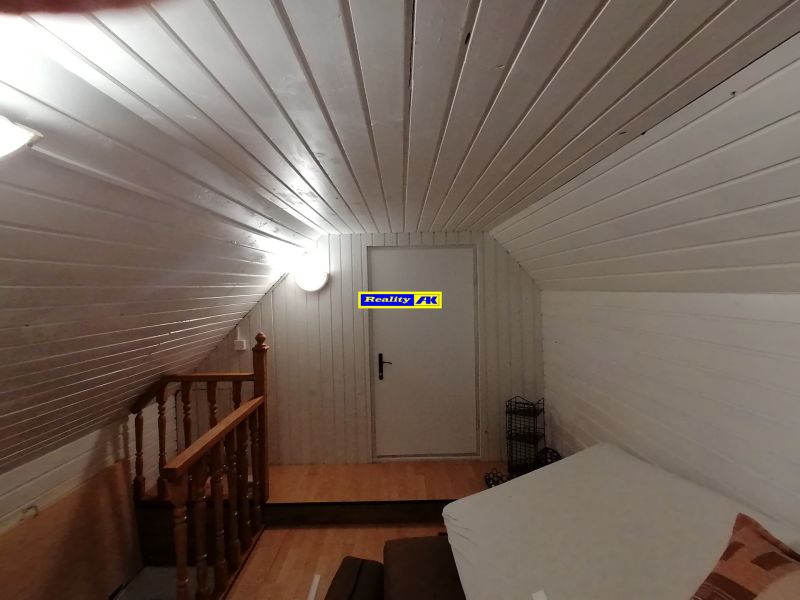 Podkrovná izba v chate s bielym drevom, gaučom a schodiskom.