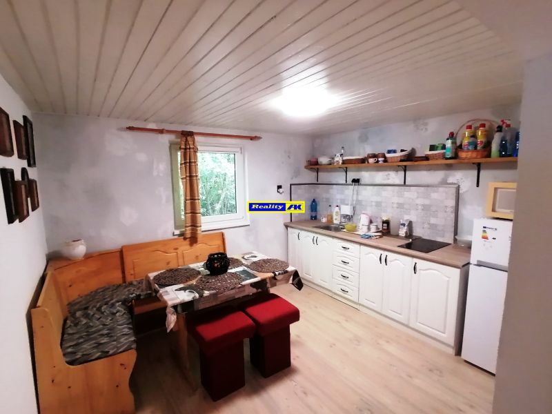 Kuchyňa v chate s posedením, bielou kuchynskou linkou, poličkami a oknom.