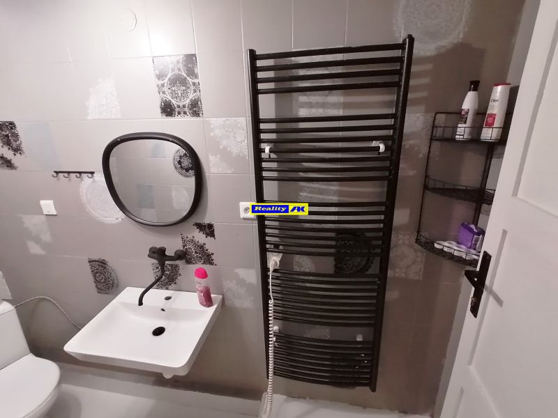 Kúpeľňa v chate so zrkadlom, umývadlom a rebríkovým radiátorom na stene.
