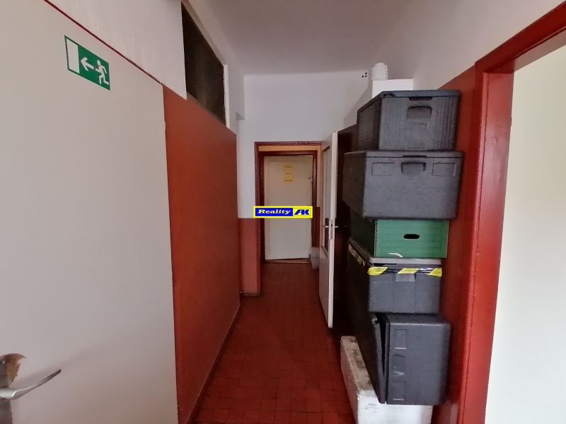 Úzky interiérový prechod s nádobami a núdzovým východom v gastro priestoroch.
