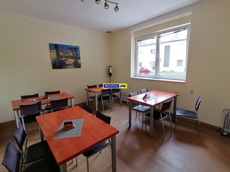 Jedáleň s červenými stolmi a obrazom na stene, podlaha s dreveným dekorom.