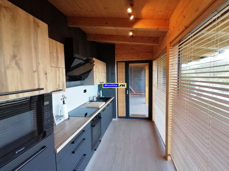 Vila s kuchyňou, drevenými skrinkami a podlahou s dreveným dekorom, výhľad cez žalúzie.