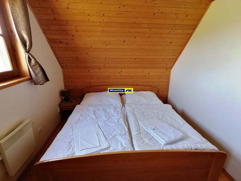 Spálňa v chate s dreveným obložením, jednoduchou manželskou posteľou a oknom.